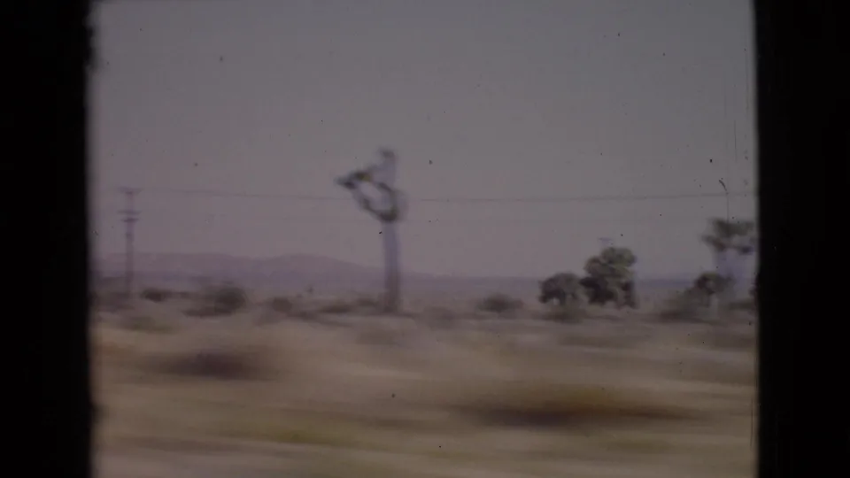 Moving 8mm view in San Diego County, 1968, with a utility pole, desert brush, scattered trees, and low hills in the distance.