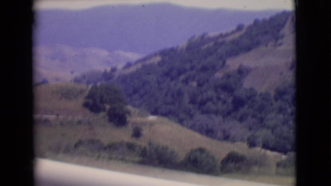 Rolling green-brown hills with tree-covered slopes and hazy distant ridges.