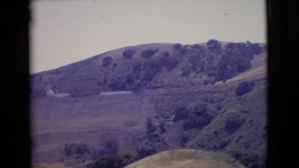 1968 San Diego County frame showing a wooded hill, open valley floor, foreground brush, and visible 8mm border edges.