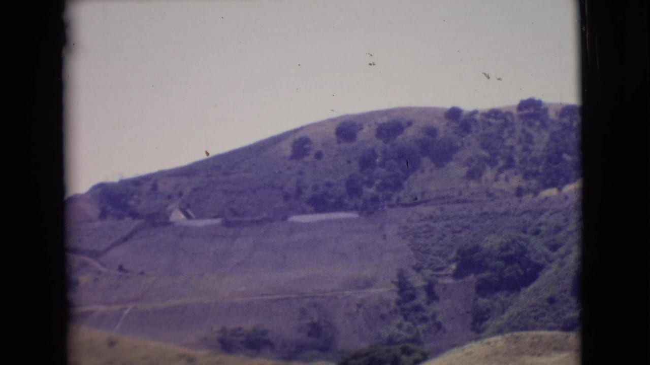 1968 San Diego County home-movie frame showing rolling hills, scattered trees, open land, and dark 8mm frame borders.