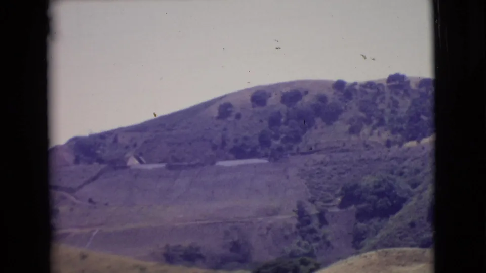 1968 San Diego County home-movie frame showing rolling hills, scattered trees, open land, and dark 8mm frame borders.