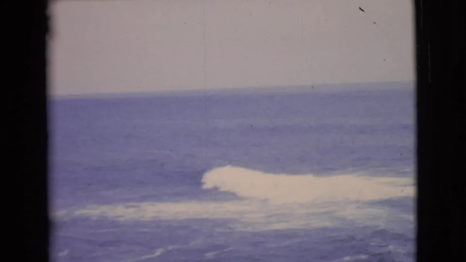 1968 San Diego County coastal frame showing blue ocean, white breaking surf, pale sky, and aged 8mm film edges.