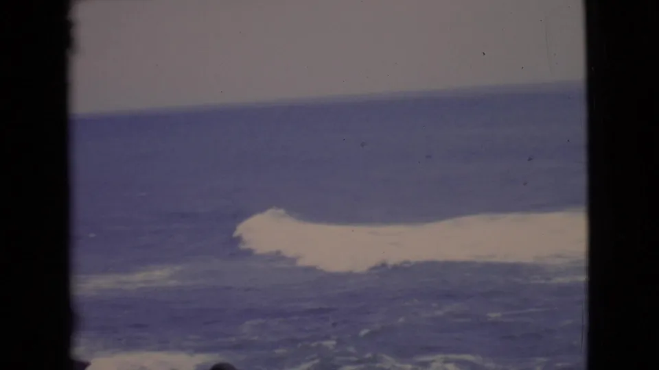 1968 San Diego County coastal frame showing a broad white wave breaking across blue water with visible 8mm grain.