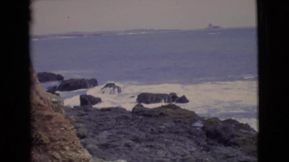 San Diego County coastal rocks and white surf appear in a faded 1968 8mm frame with the ocean stretching to the horizon.
