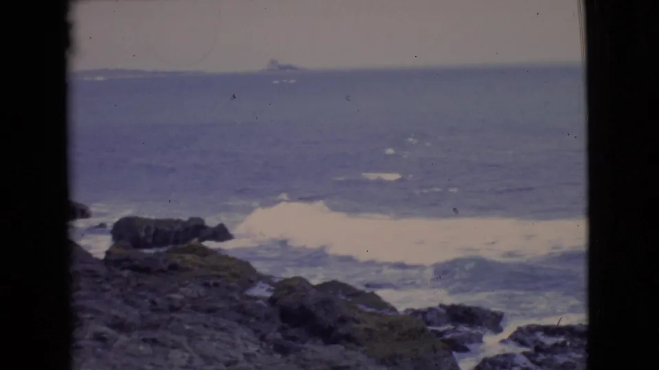 Vintage 8mm view of San Diego coastal rocks, white surf, and blue ocean from an elevated shoreline vantage point.