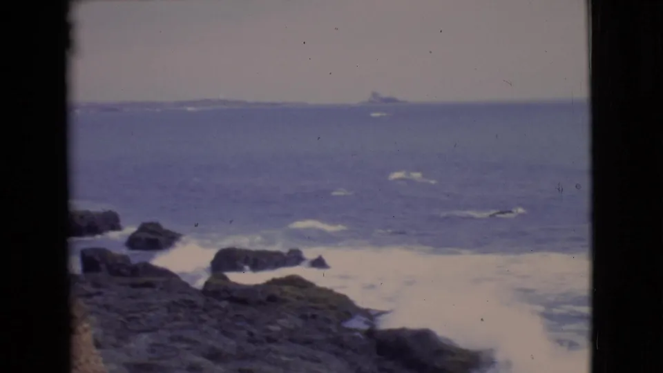 1968 8mm view of a rocky California shoreline with surf, open water, and a small distant vessel near the horizon.