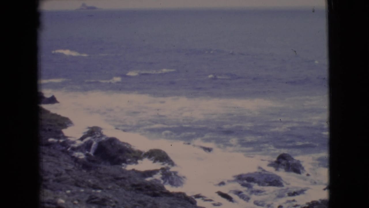 Soft 8mm frame of waves breaking over coastal rocks, likely part of the same California travel reel.