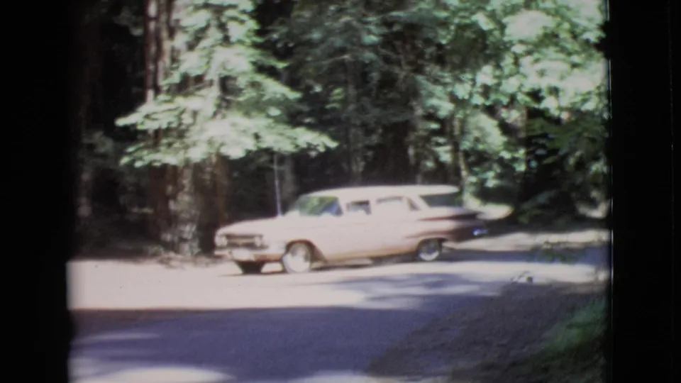 1968 San Diego County home-movie frame with a station wagon continuing along a wooded road in dappled light.