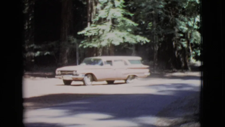 The light pink station wagon passes through a bright patch of forest road in the 1968 San Diego County home-movie footage.