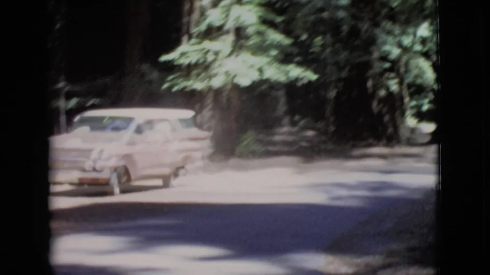 The station wagon appears motion-blurred as it arrives or turns along the San Diego County forest road in 1968 footage.