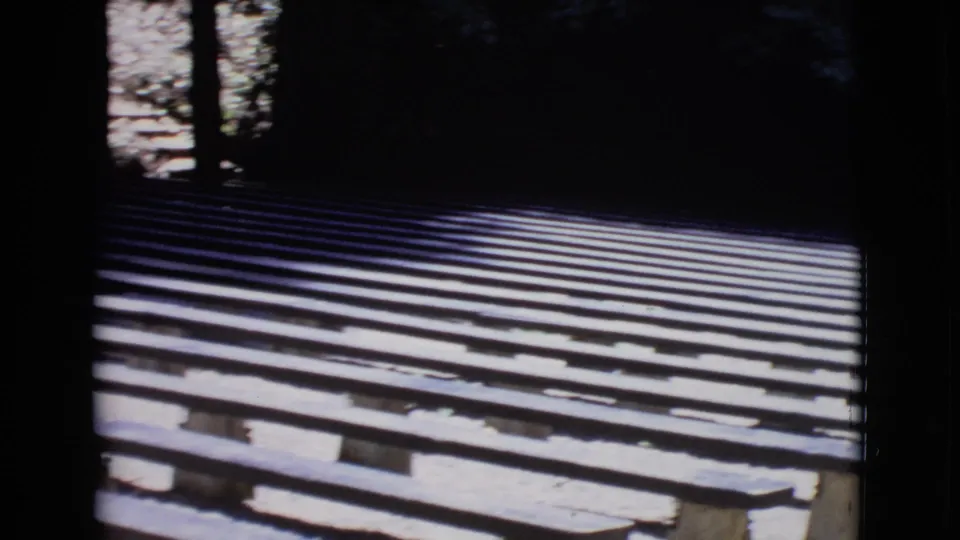 1968 San Diego County home-movie frame with empty outdoor benches, tree shadows, and bright patches of ground.