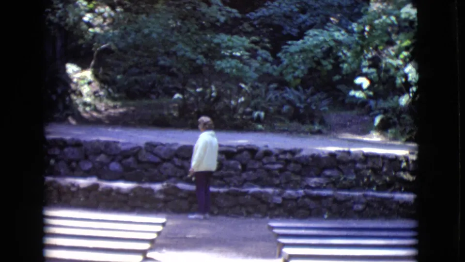 A woman in a light jacket stands in profile on a San Diego County park path, with wooden benches and dense plants visible around her.