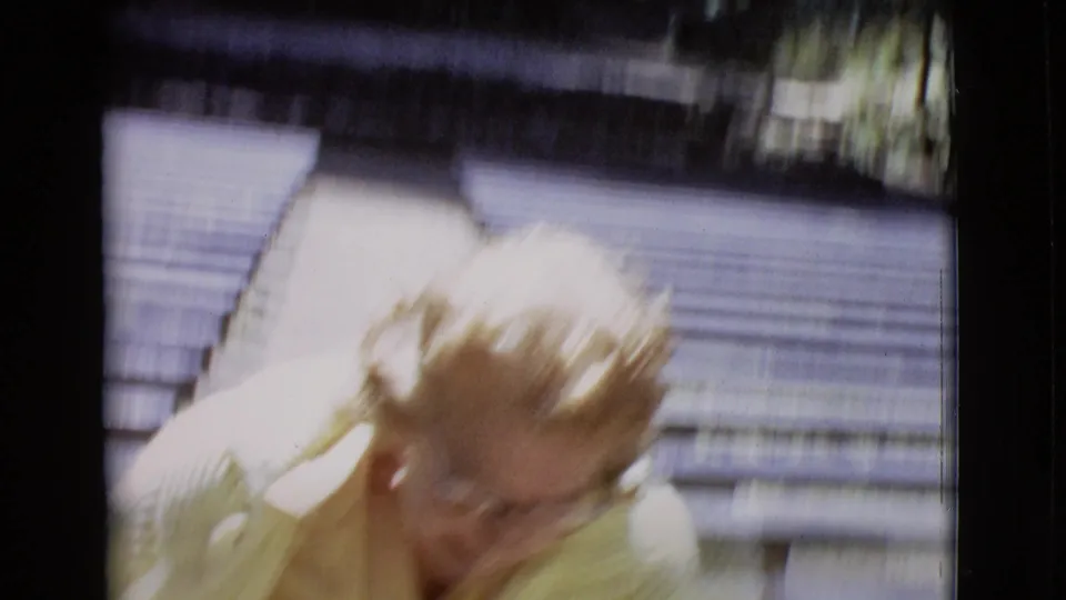 Close, blurred 1968 home-movie frame of the woman in a yellow jacket as she approaches or passes the camera in the park.