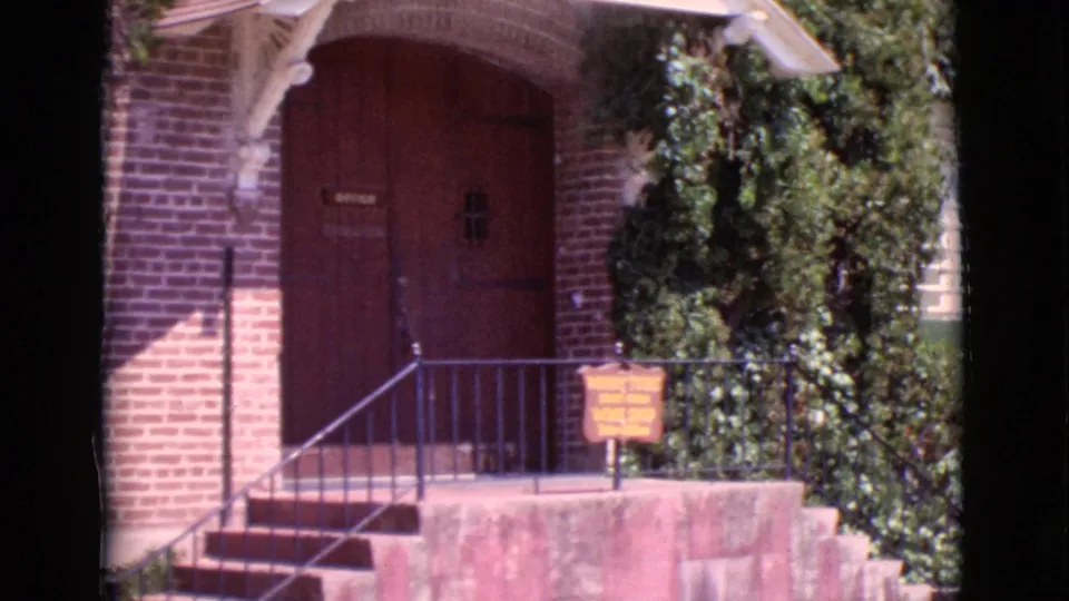 1968 San Diego County 8mm frame showing a brick building entrance with arched red doors, steps, railing, ivy, and a small sign.