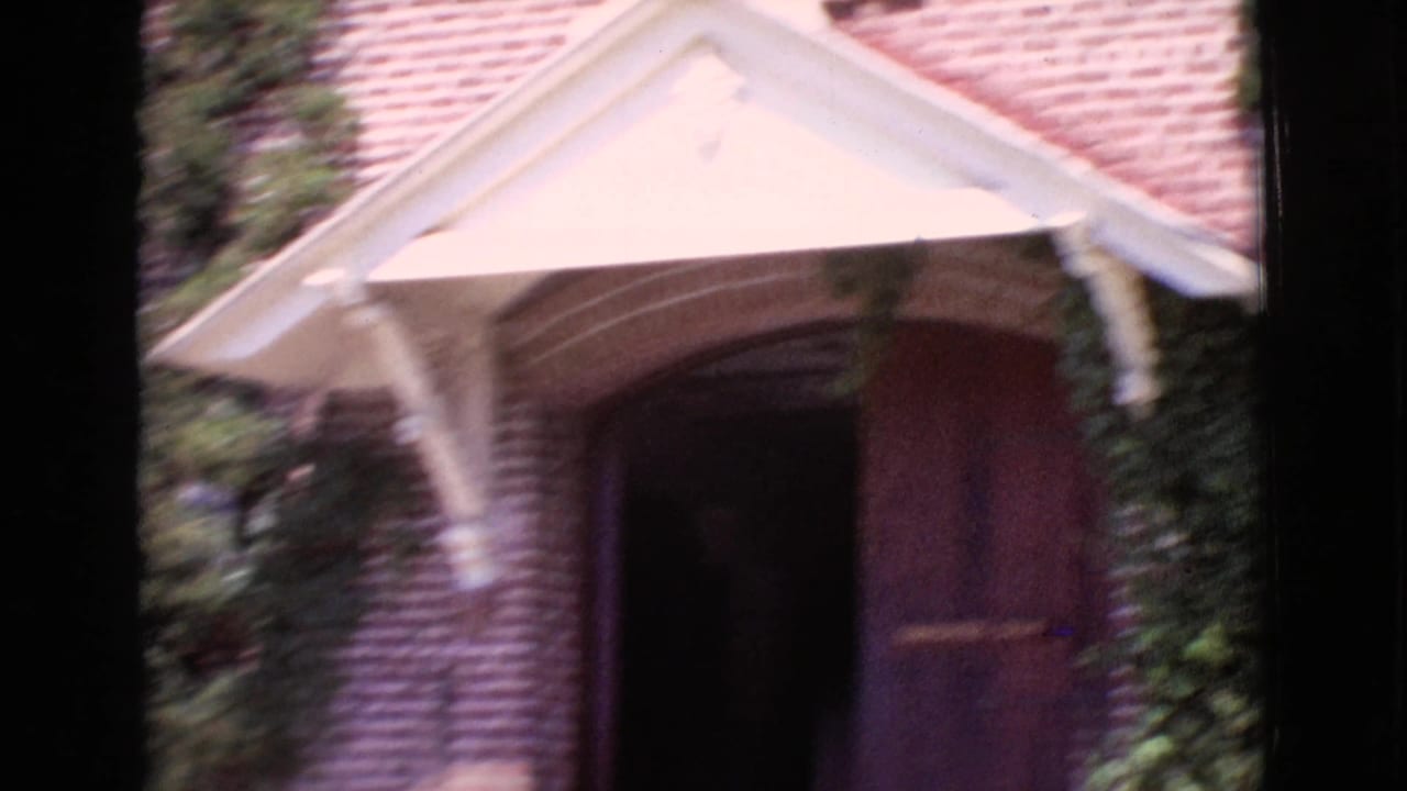 Brick building entrance with white awning, arched doorway, and ivy at the edge of the frame.