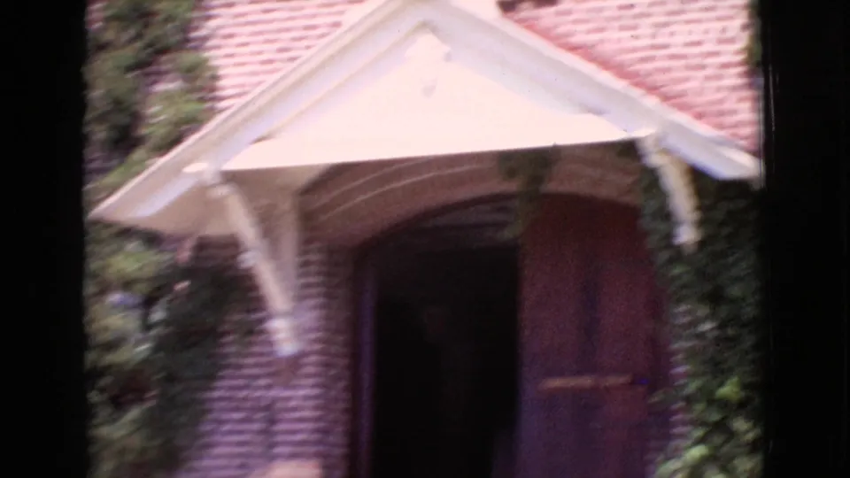1968 San Diego County 8mm frame showing a brick building entrance with a white awning, dark wooden door, and surrounding ivy.