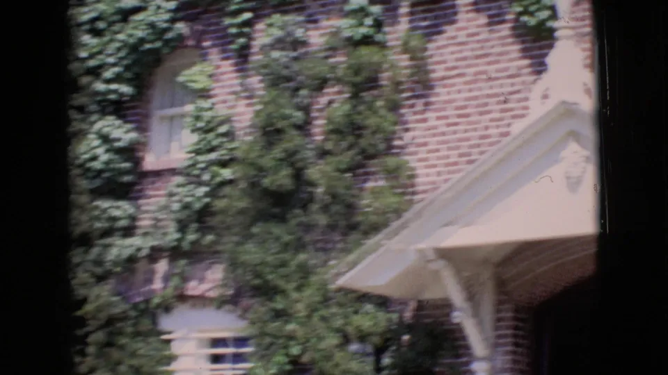 1968 San Diego County home-movie frame of an ivy-covered brick facade with small windows and a white awning along the edge.
