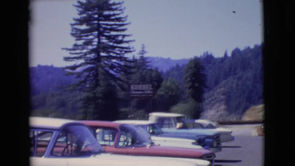 1968 8mm view of cars parked near a scenic road in San Diego County, with wooded hills and KORBEL signage behind them.