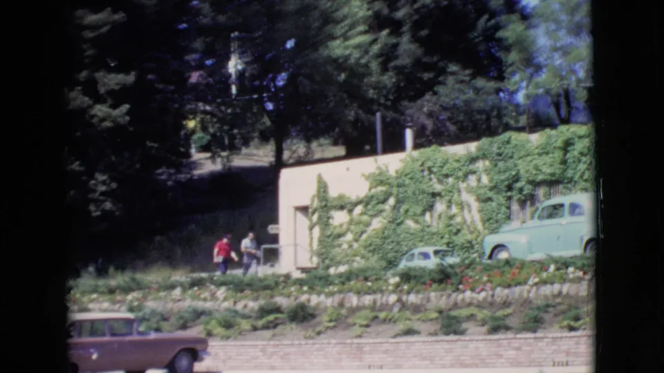 A 1968 San Diego County 8mm frame shows two men on a landscaped slope near a pale green sedan and an ivy-covered building.