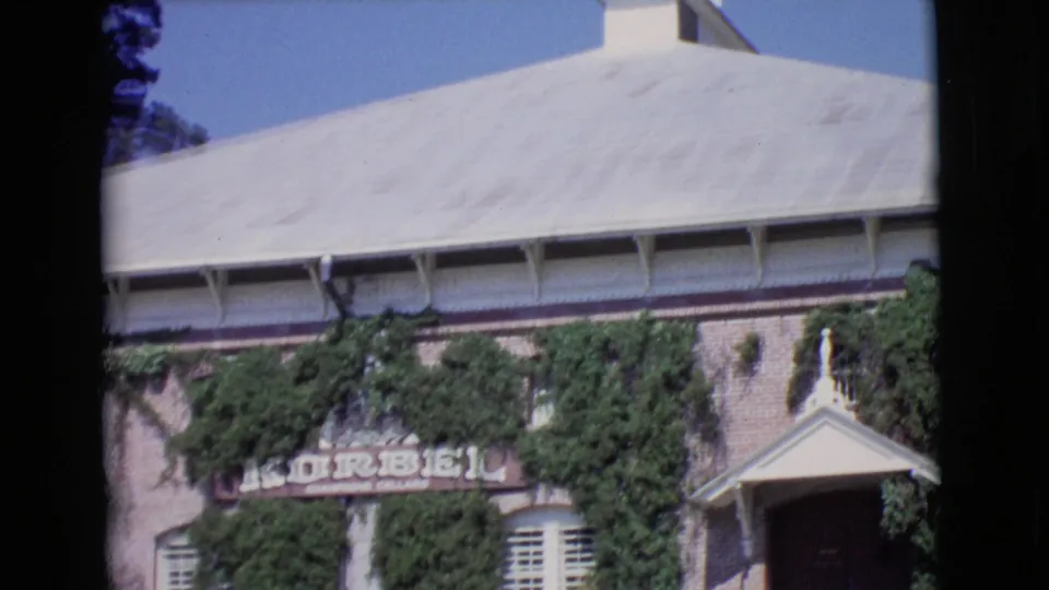 1968 San Diego County frame with the Korbel sign partly centered on an ivy-covered brick building beside white shutters and an entrance porch.