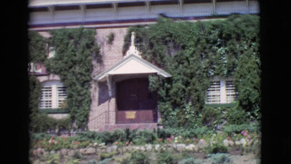 1968 San Diego County frame focusing on the porch, shuttered windows, dense ivy, brick wall, and landscaped flower bed outside the building.