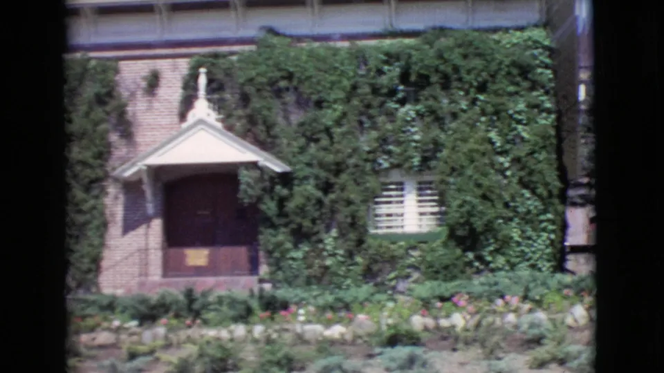 1968 San Diego County 8mm frame showing an ivy-covered brick exterior with a small gabled entrance, shuttered window, and landscaped garden.