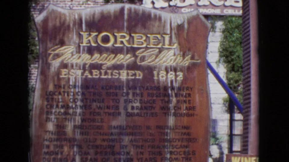 1968 San Diego County home-movie frame of the Korbel Champagne Cellars sign, with blue handrail and surrounding building details visible.