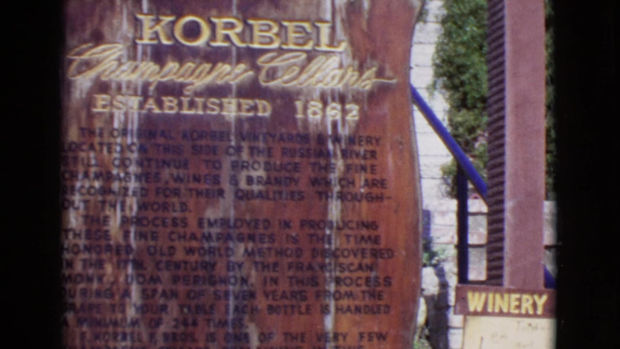 1968 8mm frame showing a weathered Korbel Champagne Cellars informational sign with gold lettering and a small winery sign nearby.