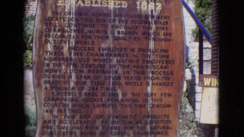 1968 home-movie frame showing more of the winery monument text, with worn lettering, stone surroundings, and a partial winery sign.