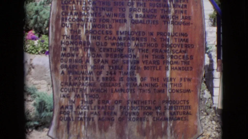 1968 San Diego County 8mm frame centered on a weathered Korbel winery plaque with landscaping visible behind it.