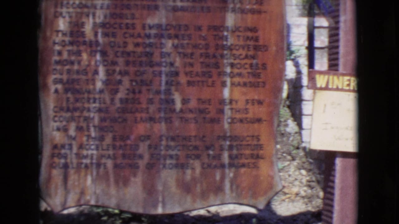 1968 San Diego County 8mm frame showing a weathered brown Korbel process sign beside a partial white winery sign outdoors.