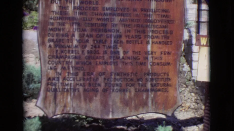Close 8mm view of the brown champagne production sign in San Diego County, with plants and a partial winery sign near the edge.