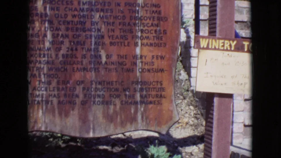 1968 San Diego County 8mm frame showing the Korbel-related process sign beside a white winery sign and exterior wall.