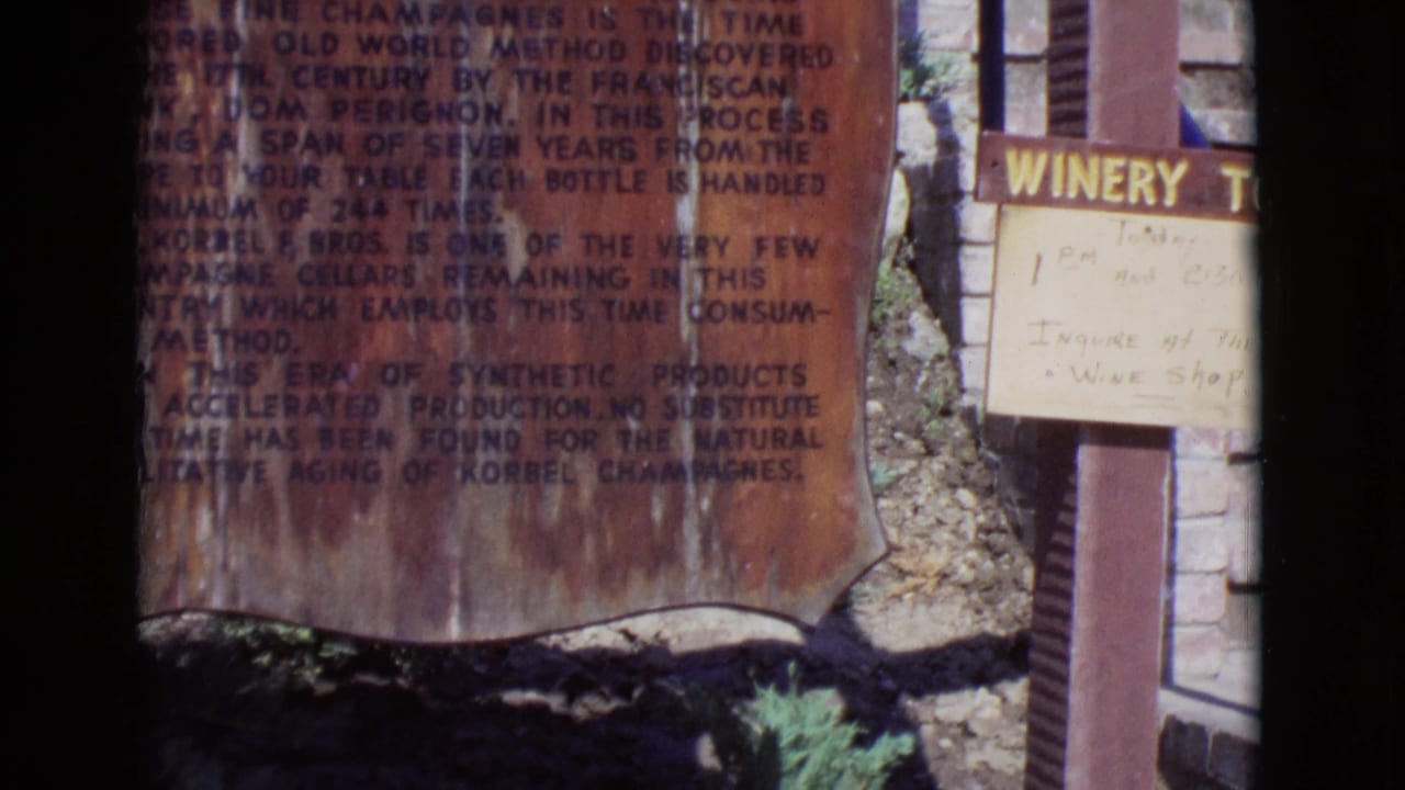 1968 San Diego County home-movie frame showing a close view of signage near a winery entrance, with a partial doorway and dark film border.