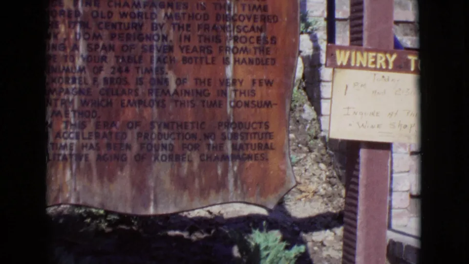 1968 San Diego County home-movie frame showing a close view of signage near a winery entrance, with a partial doorway and dark film border.