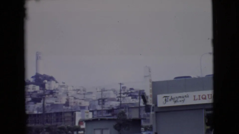 1968 San Diego County view of a hillside town with a prominent white tower, utility poles, commercial rooftops, and a Fisherman's Wharf liquor sign.