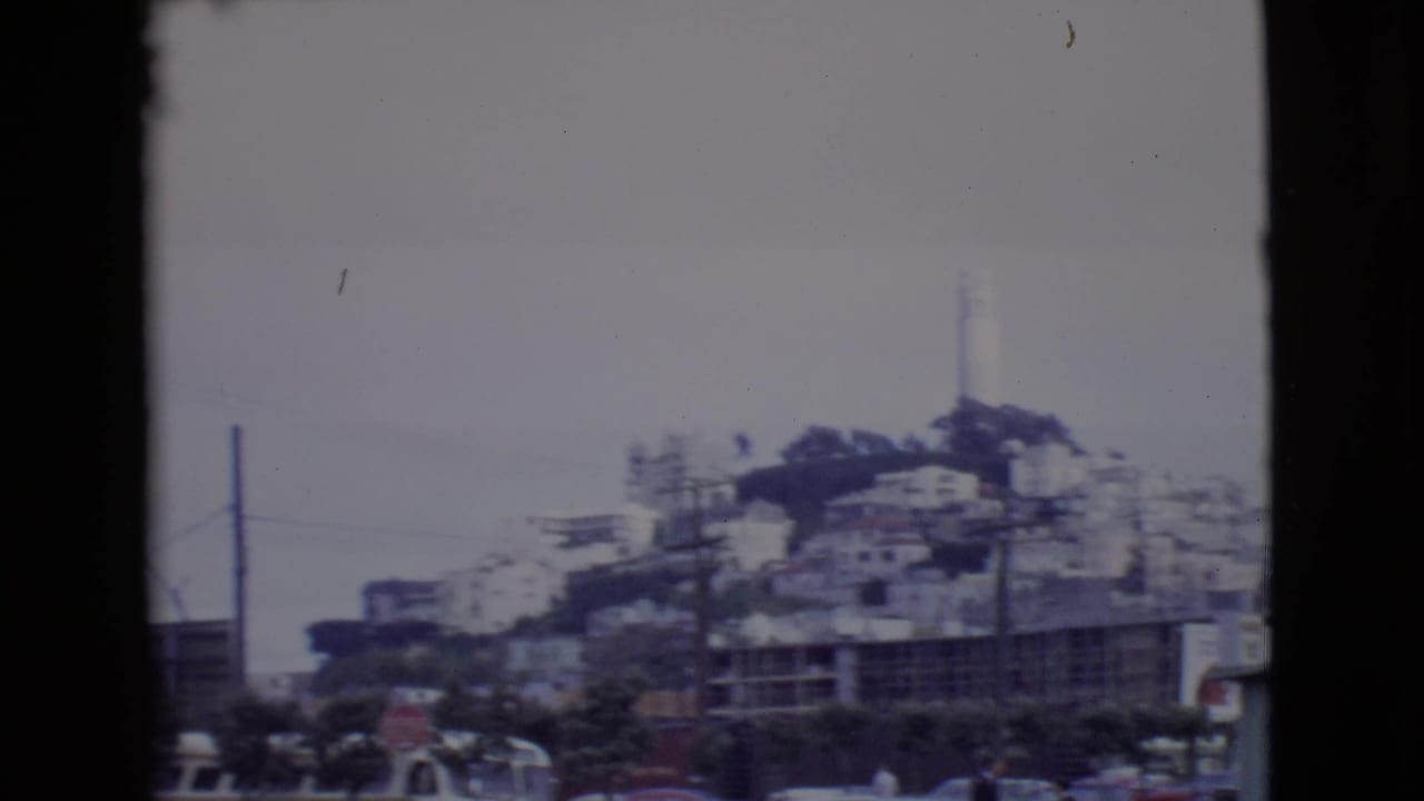 Hillside neighborhood with a white tower above a street, seen through dark frame edges.