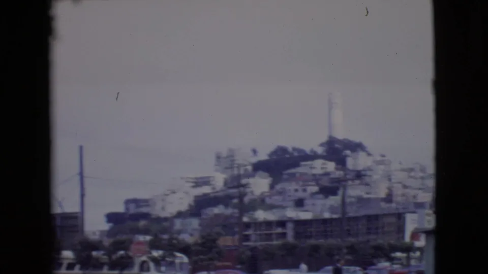 1968 San Diego County home-movie view of a hillside with a white tower, low buildings, utility poles, and street traffic below.