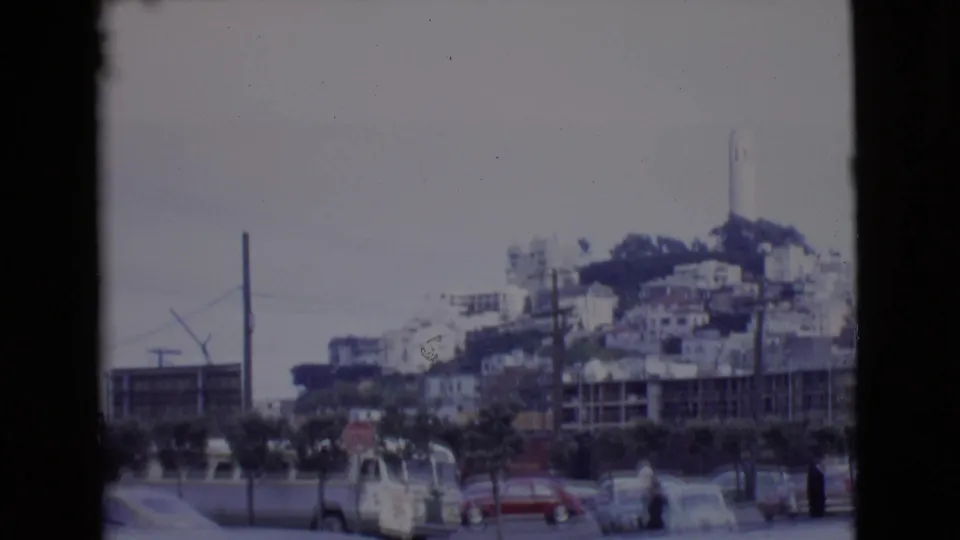 San Diego County hillside view with a white tower, clustered buildings, utility poles, cars, and a small pedestrian figure near the street.