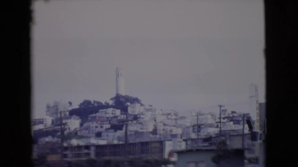Final 1968 San Diego County frame with a white tower on the hill, hillside buildings, power poles, and a partial street scene below.