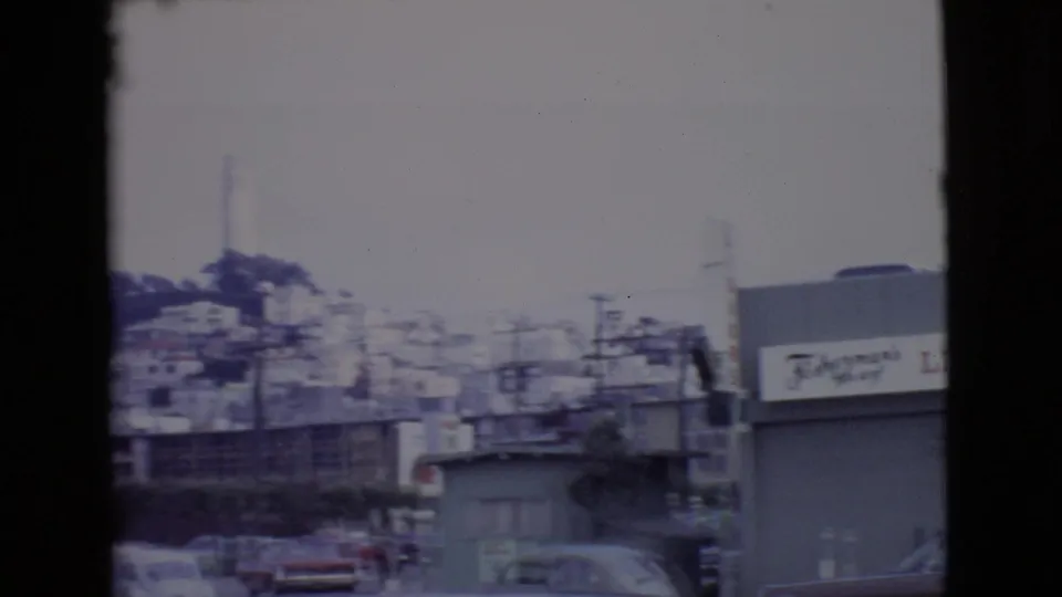 1968 San Diego home-movie frame showing a waterfront street area with low buildings, distant cars, utility poles, and soft film exposure.