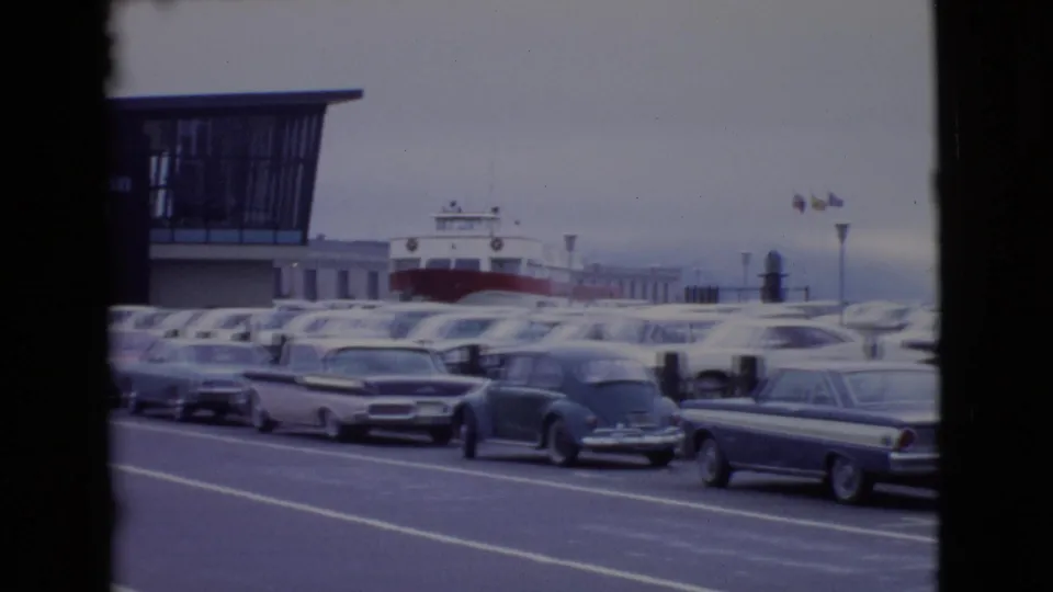 1968 San Diego waterfront frame with mid-century cars lined near a ferry terminal and a docked ferry visible in the background.