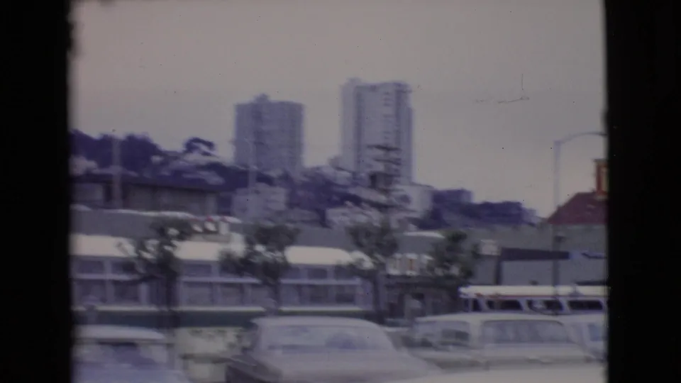 1968 San Diego County street scene with mid-century cars, green-and-white buses, commercial buildings, and apartment towers on a hillside.