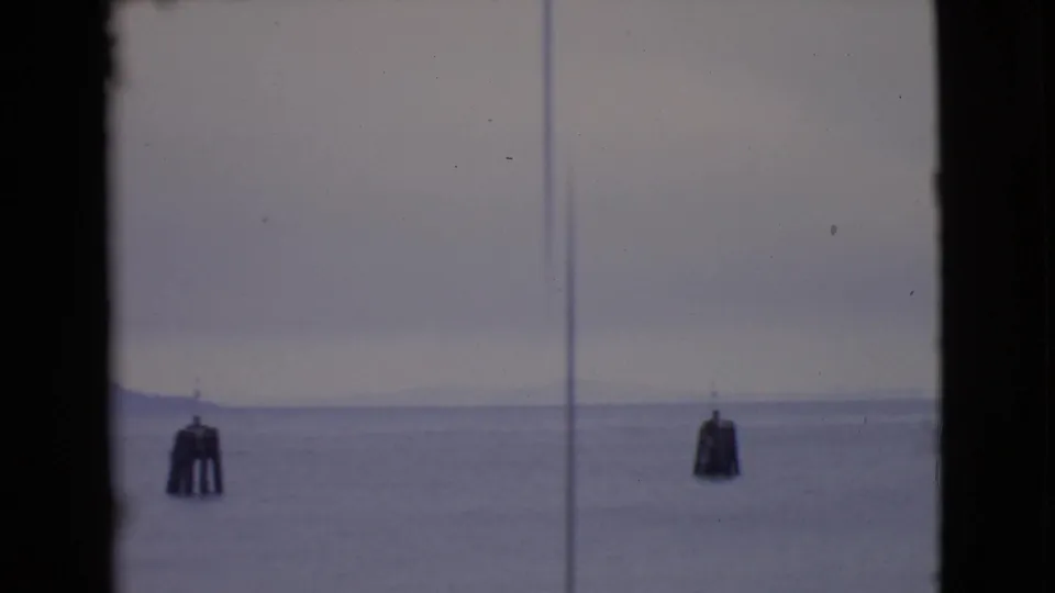Quiet San Diego County waterfront view on 8mm film, showing open water, a buoy, hazy sky, and a distant shoreline or low landform.