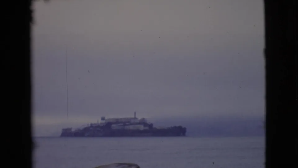 Soft 8mm frame of a foggy island complex across San Francisco Bay, with water and dark film-gate edges visible.