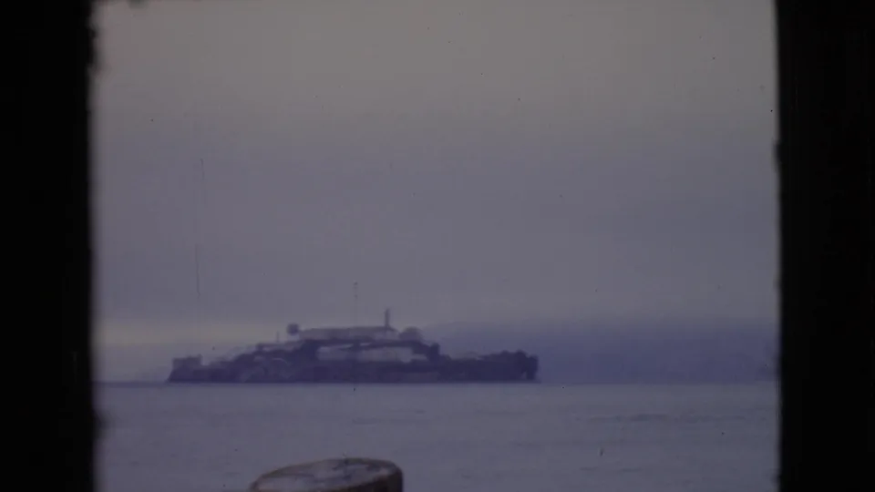 1968 8mm home-movie frame showing a distant foggy island complex across calm San Francisco Bay water.