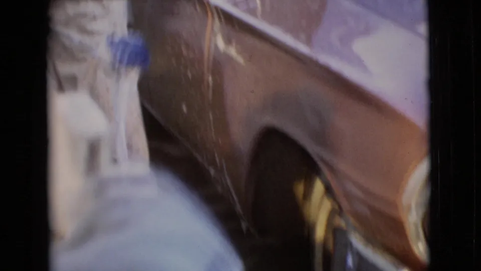 Close 8mm view of soapy water and reflections on the side of a gold-colored classic car during washing.