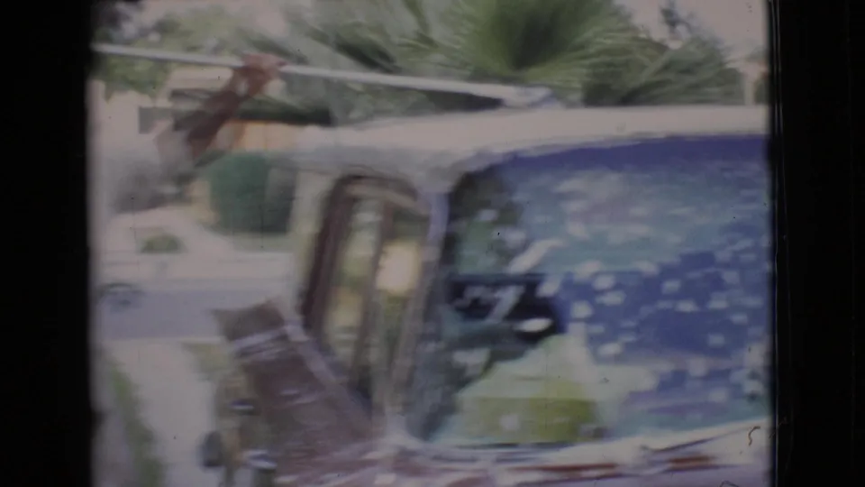 The brush moves across the soapy roof and windshield area of a classic car in bright suburban light.