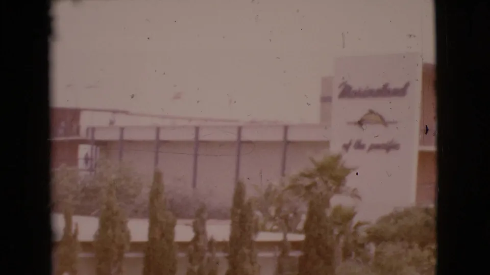 A soft 8mm view shows the Marineland of the Pacific sign on a building exterior, with shrubs and palms in front.
