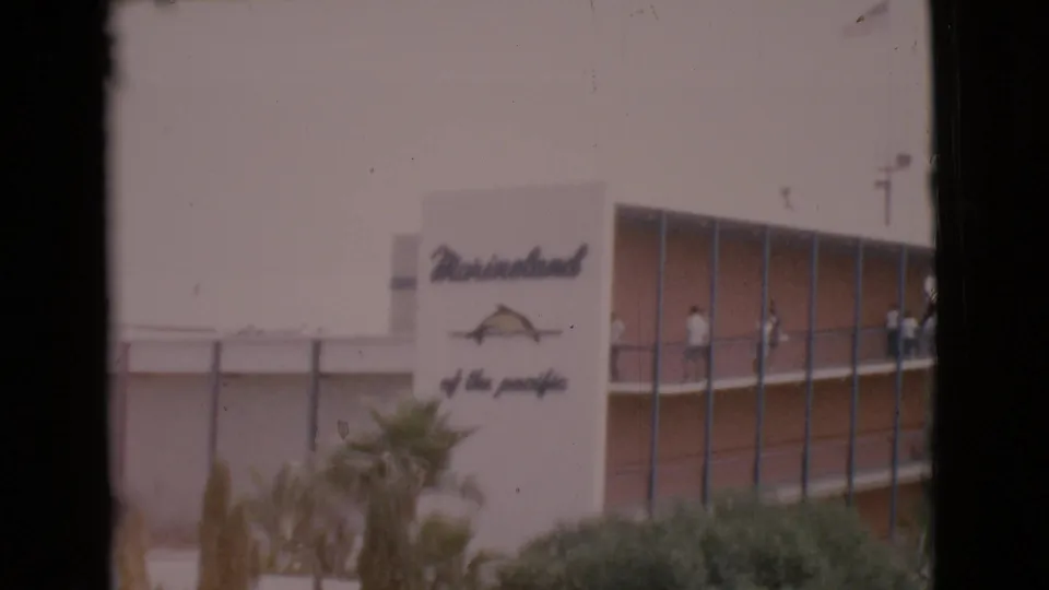 A faded home-movie frame shows the Marineland sign, palm landscaping, glass windows, and small figures standing along a balcony.